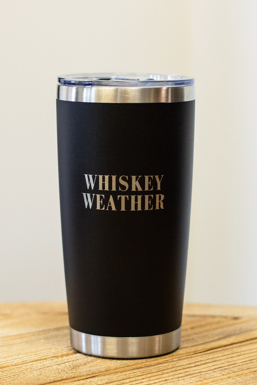 The 20oz Whiskey Weather Tumbler by Panache Apparel Collection features a sleek black design with bold silver lettering and a clear lid—perfect for stylishly enjoying your favorite drink.