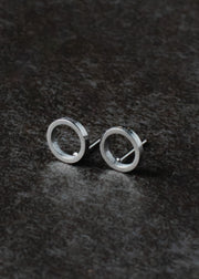 The Begin Again Stud Earrings - Silver by panacheaccessories are minimalist open circle studs, crafted from lead and nickel free stainless steel, shown on a dark textured surface.