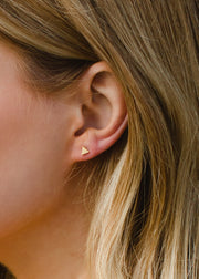 Close-up of a persons ear with straight, light brown hair wearing panacheaccessories Scout Stud Earrings - Gold, small gold triangle studs that are perfect for anyone seeking hypoallergenic earrings.