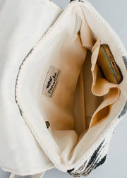 The Camilla Backpack by Panache Apparel Collection, shown from above, features cream-colored cotton fabric, adjustable straps, multiple inner pockets (one holding a bronze phone), and a visible Pursche label.