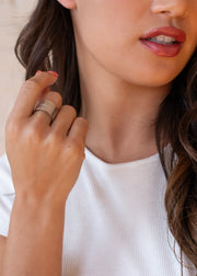 A woman with wavy brown hair in a white ribbed top shows off the Luxe Silver Textured Ring by panacheaccessories. Her lips are parted, nails painted pink, with the image cropped to reveal her face, hand, and upper torso.
