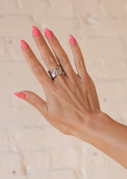 A hand with long, glossy pink nails is shown against a light background. The middle finger showcases the Luxe Silver Wide Hammered Ring by panacheaccessories, a chunky adjustable stainless steel piece that adds a modern touch.