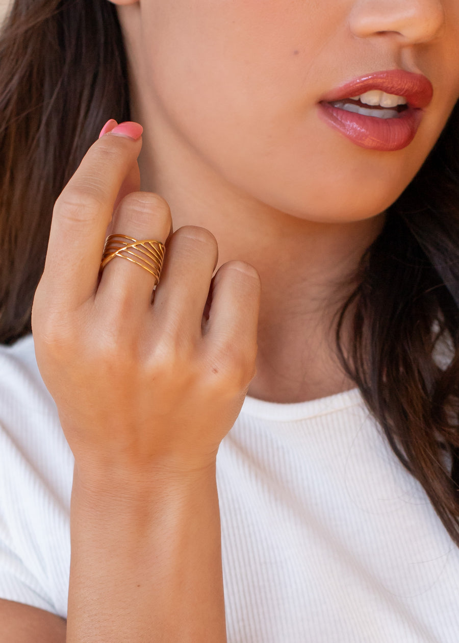 A woman in a white shirt displays her manicured hand adorned with the Luxe Gold Multi-Strand Ring by panacheaccessories, featuring an intricate 18K gold design, as her lips are slightly parted.
