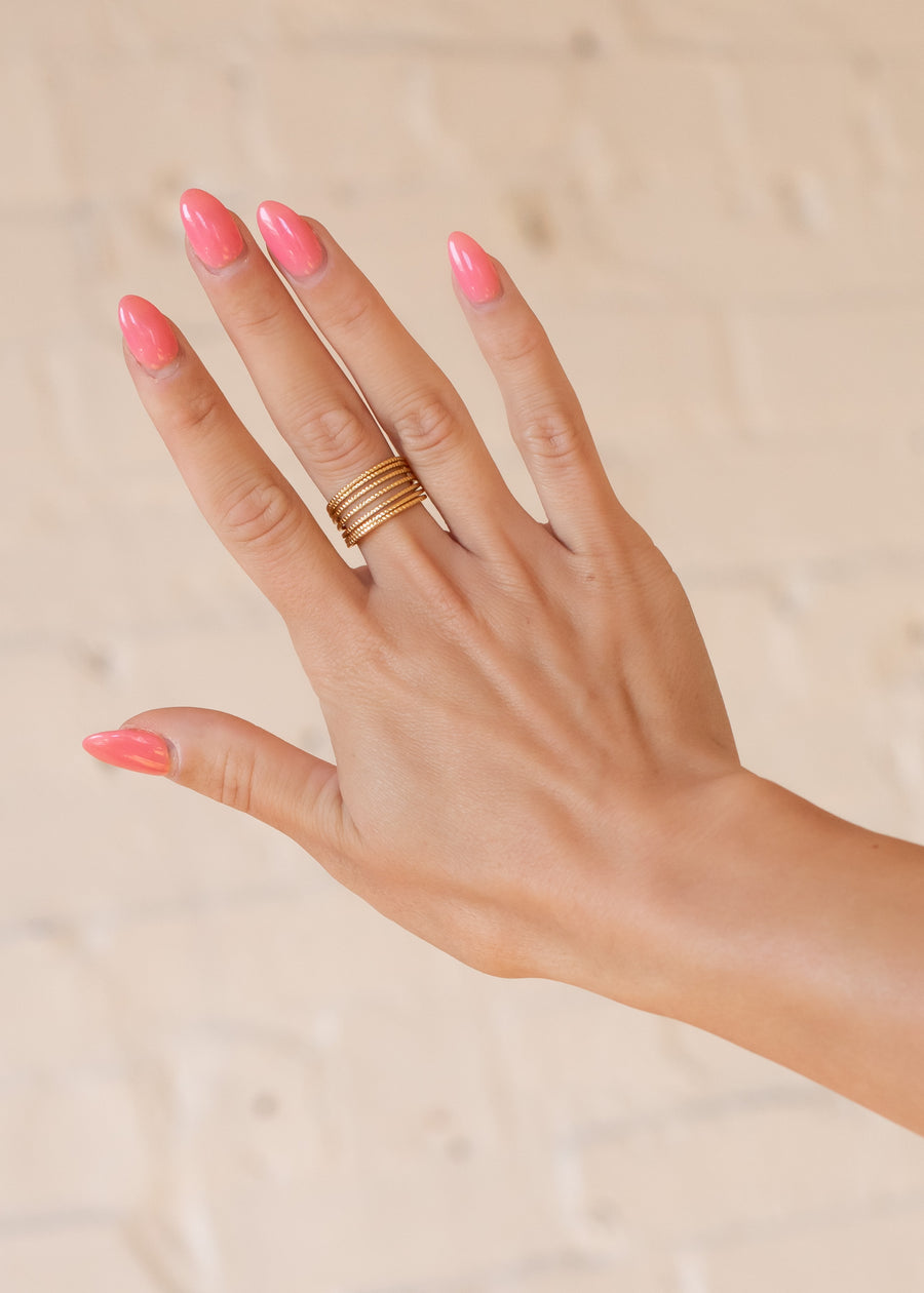 A hand with long, glossy pink nails is shown against a light background, wearing the Luxe Gold Dainty Multi-Strand Ring by panacheaccessories on the middle finger.