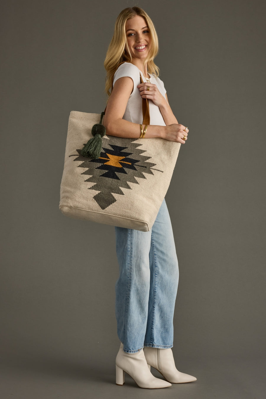 Woman holding a beige tote bag with a geometric pattern against a gray background