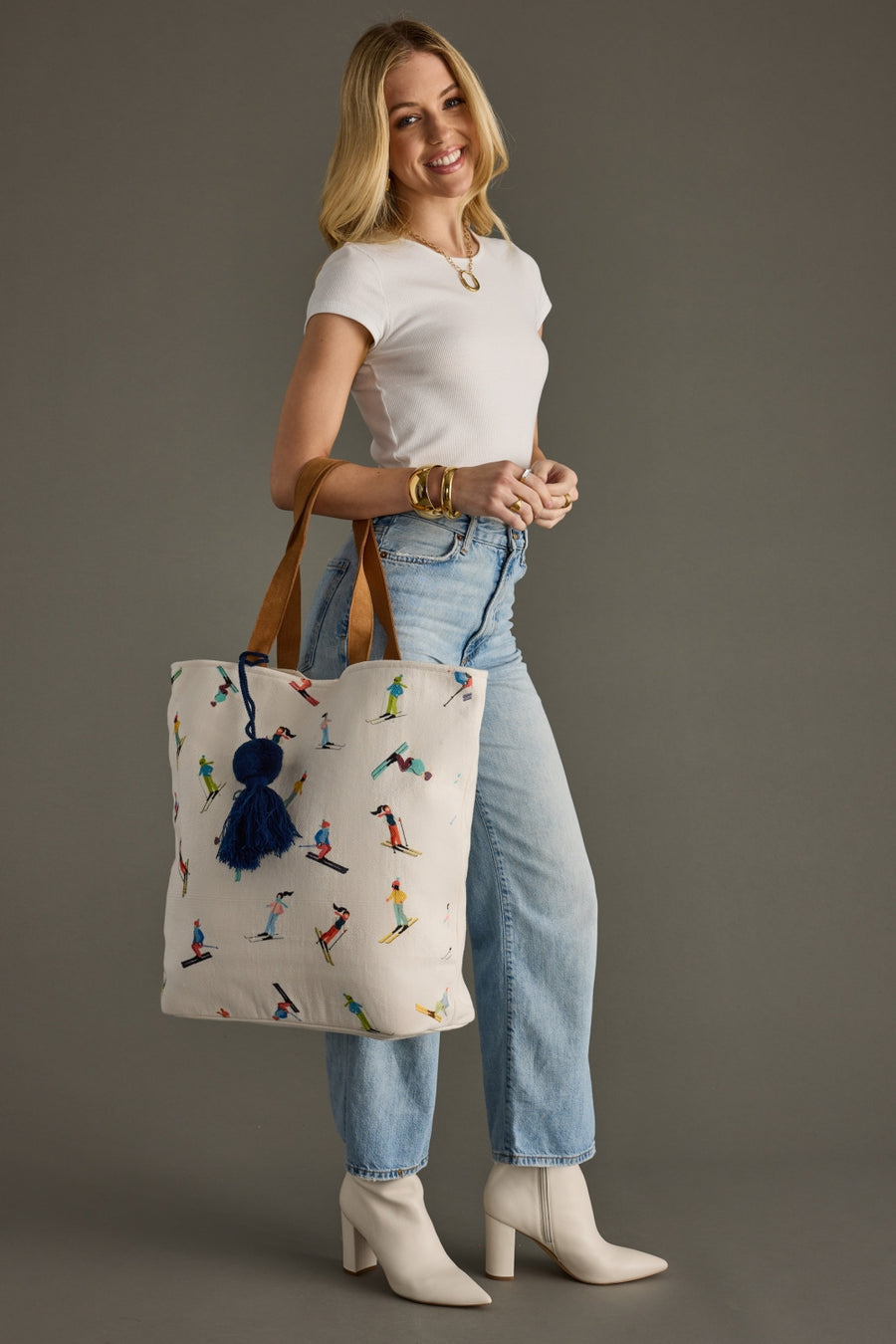 Woman holding a tote bag with a pattern of people skiing against a gray background