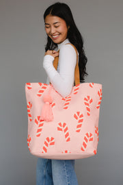 Woman holding a pink tote bag with candy cane pattern and tassel on a gray background