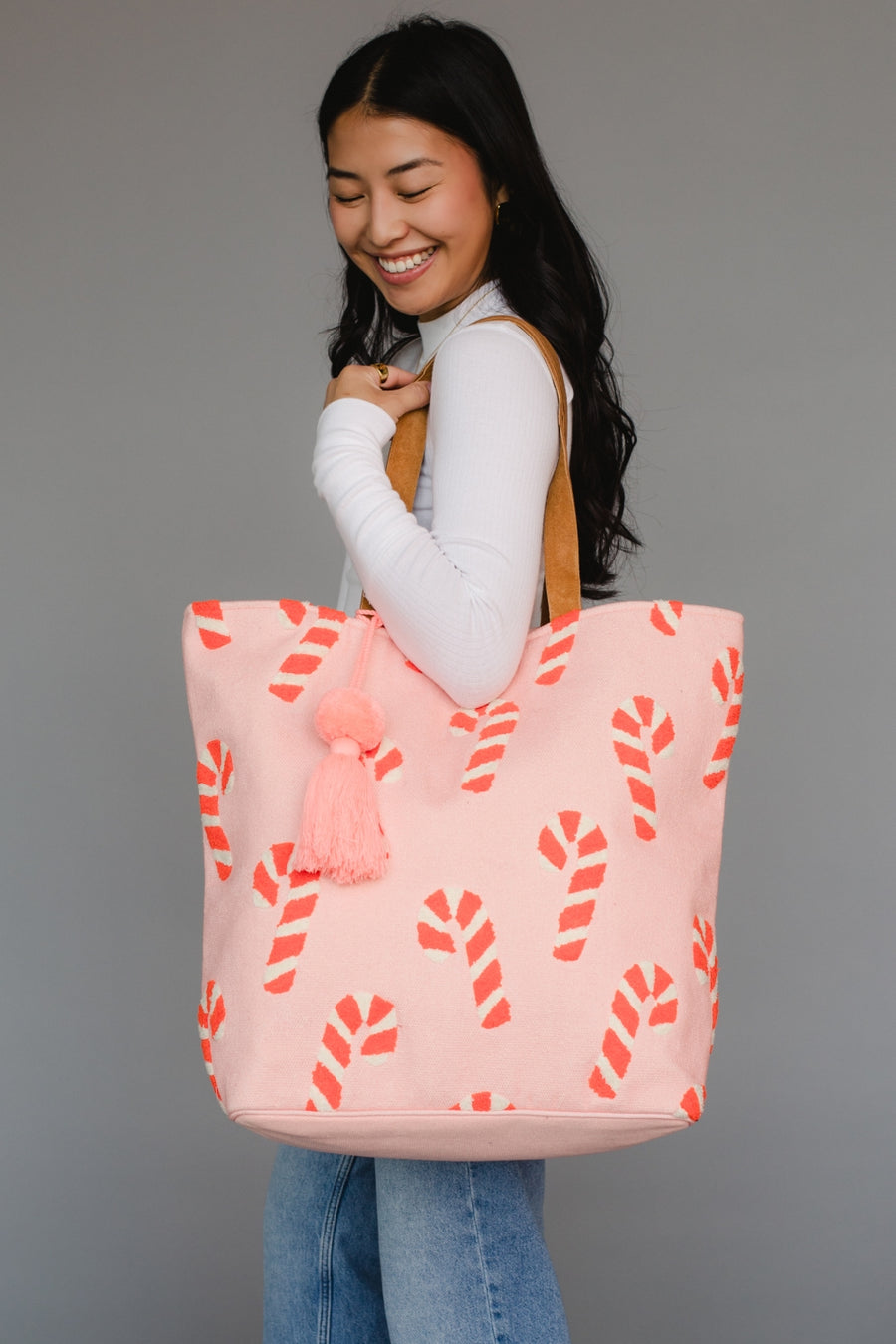 Woman holding a pink tote bag with candy cane pattern and tassel on a gray background
