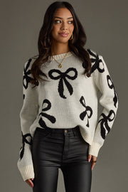 Woman wearing a white sweater with black bow patterns against a gray background