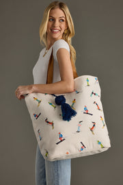 Woman holding a tote bag with skiing designs and a blue tassel against a gray background