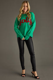 Woman wearing a green sweater with 'jolly' text, black pants, and high heels on a gray background