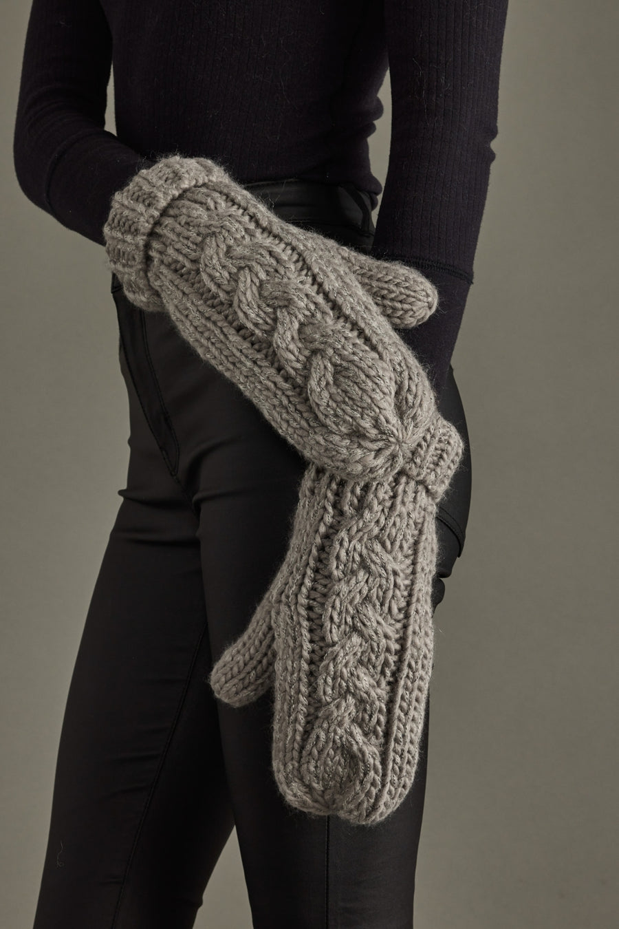 Person wearing gray knit mittens against a neutral background