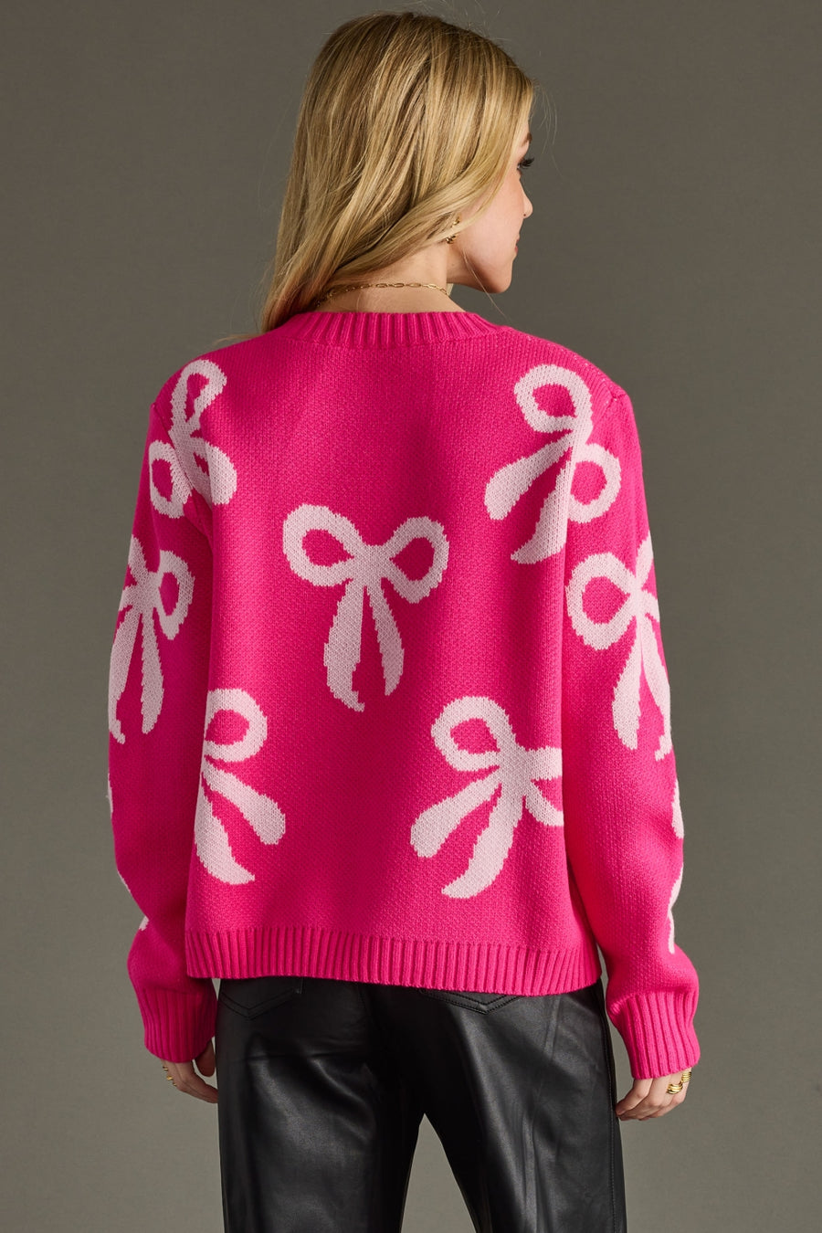 Person wearing a bright pink sweater with white bow patterns on a gray background