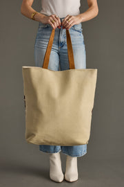 Person holding a beige tote bag with brown handles against a gray background