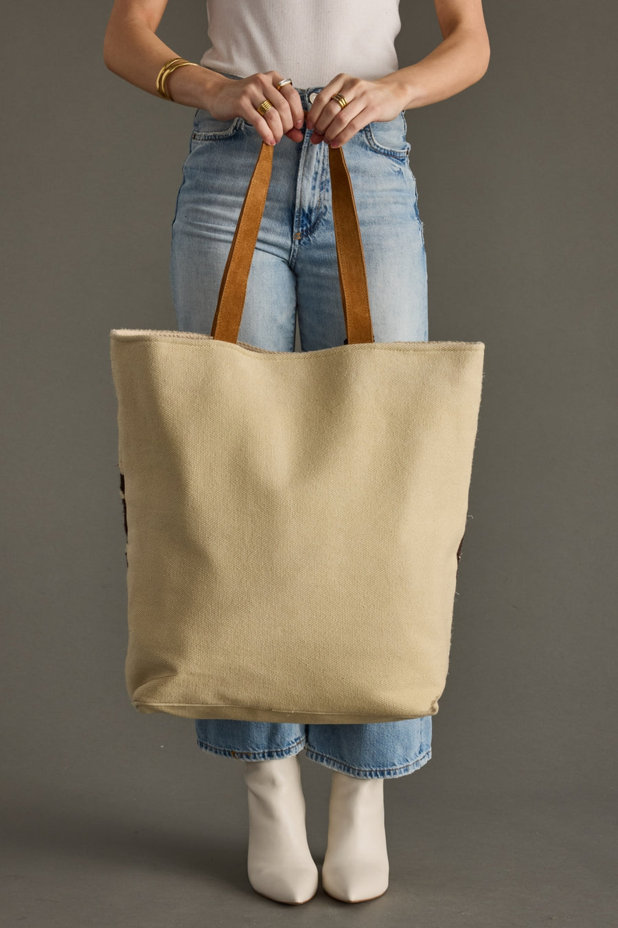 Person holding a beige tote bag with brown handles against a gray background