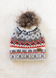 Knitted hat with a pattern and fur pom-pom on a white background