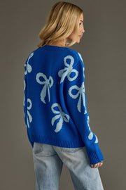 Person wearing a blue sweater with white bow patterns on a gray background
