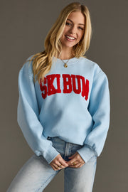 Woman wearing a light blue sweatshirt with 'SKI BUM' in red text on a plain background