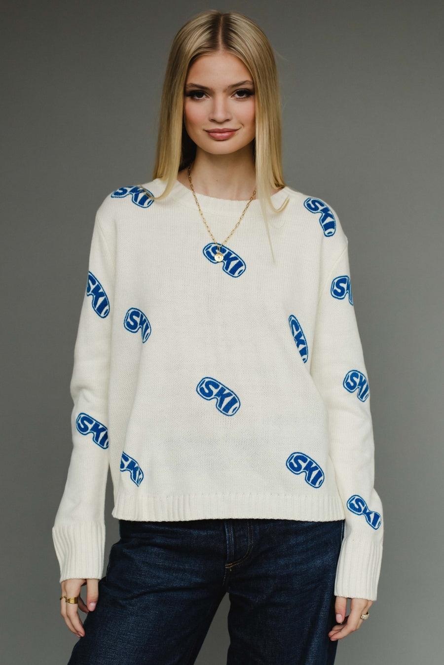 Woman wearing a white sweater with blue logos on a gray background
