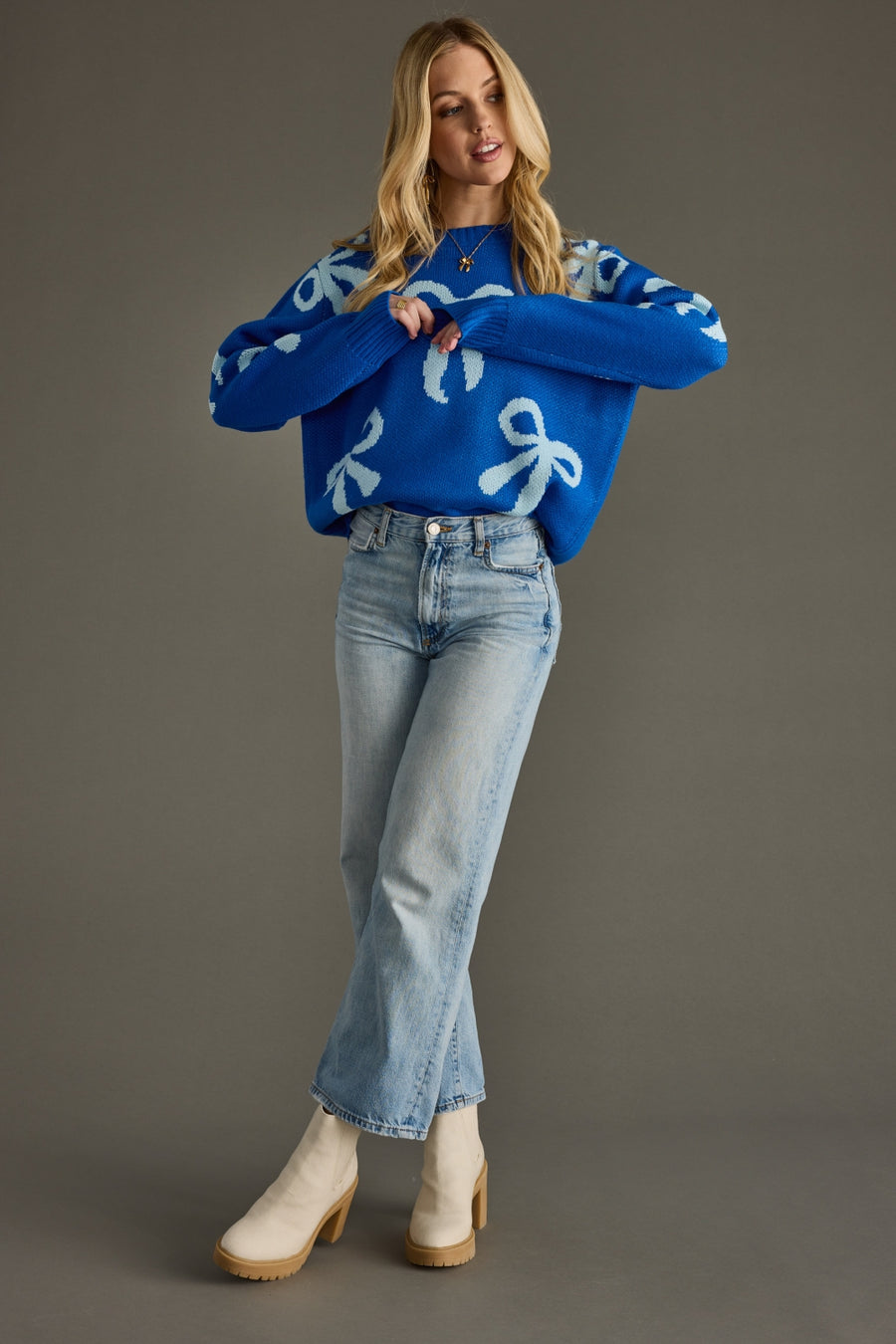 Woman wearing a blue sweater with white patterns and jeans on a gray background