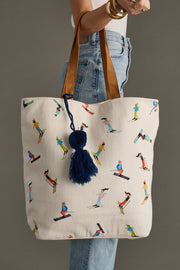 Tote bag with skiing pattern and navy pom-pom held by a person wearing jeans and a white top.