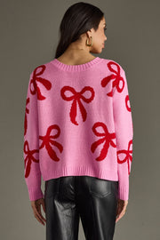 Person wearing a pink sweater with red bow patterns on a gray background