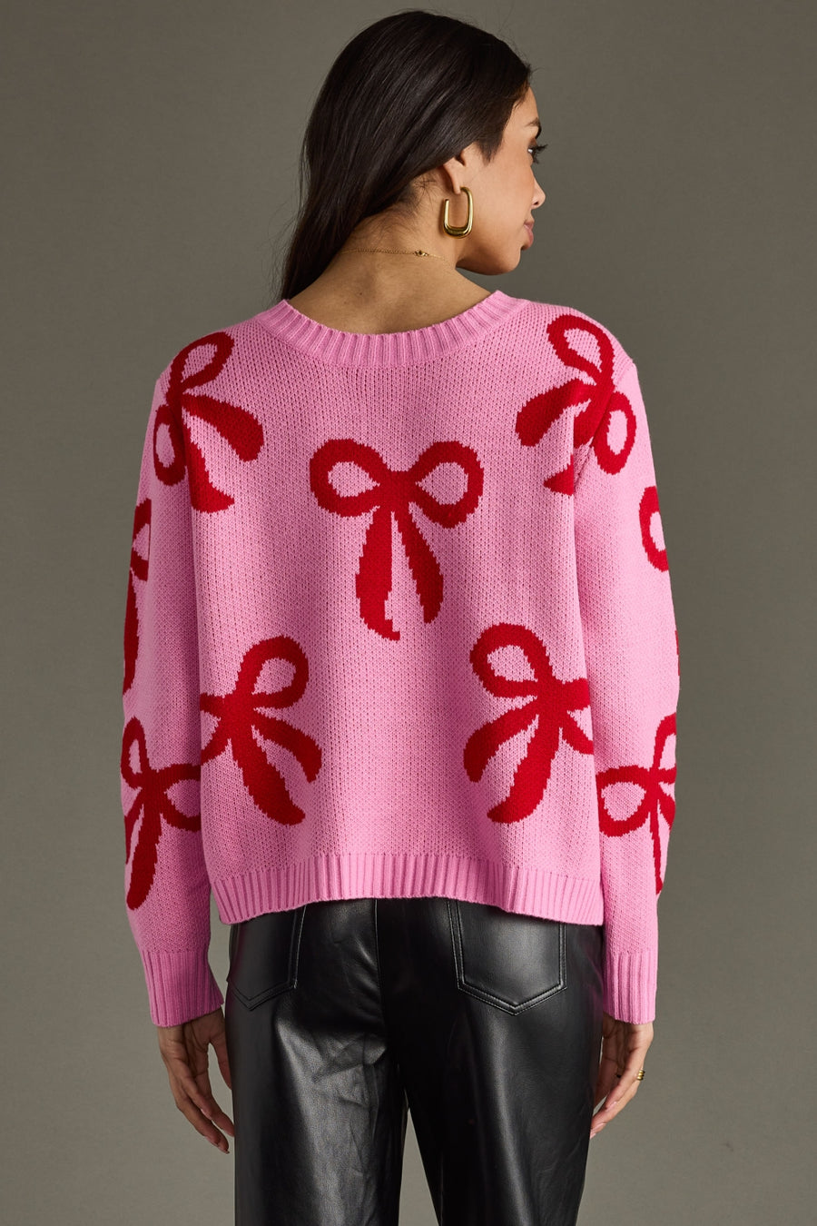 Person wearing a pink sweater with red bow patterns on a gray background