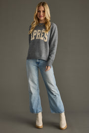 Woman wearing a gray sweater with 'APRES' text and blue jeans on a gray background