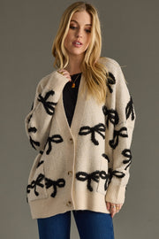 Woman wearing a cream cardigan with black bow patterns on a gray background