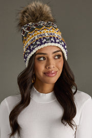 Woman wearing a colorful knit beanie with a fur pom-pom on a gray background