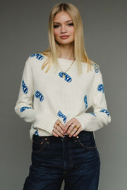 Woman wearing a white sweater with blue patterns on a gray background