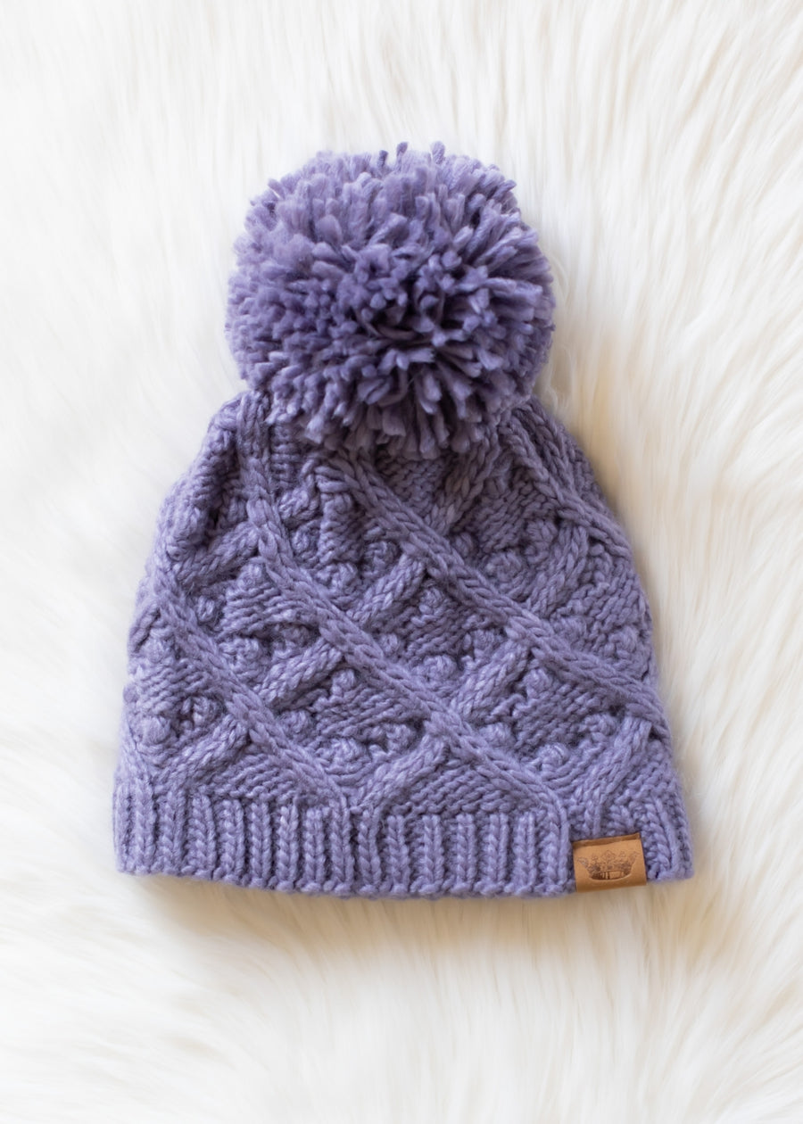 Purple knitted beanie with a pom-pom on a white background