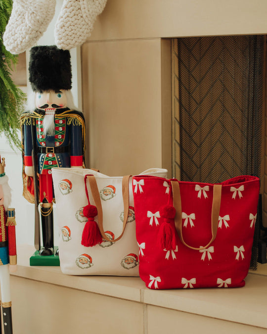 A smiling woman in a red ho ho ho sweater and black skirt holds a champagne glass, standing in front of a decorated Christmas tree.