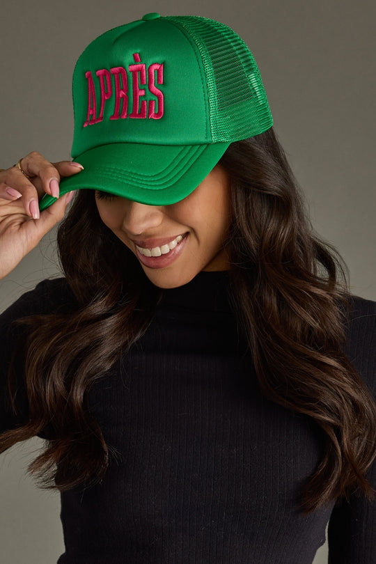 Woman wearing a green cap with 'APRèS' text, smiling against a neutral background