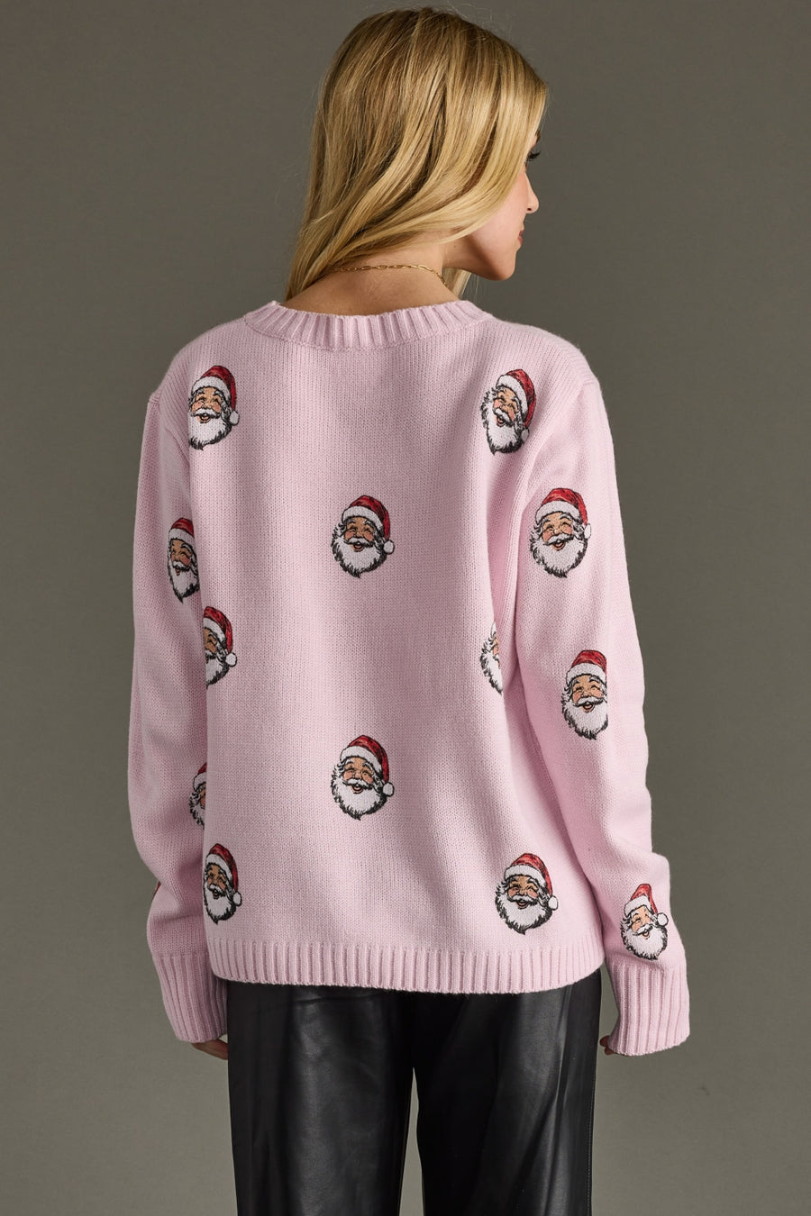 Pink sweater with Santa Claus patterns worn by a person on a gray background