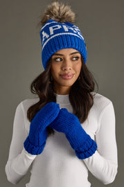 Woman wearing a blue knit beanie and gloves with a brand logo on a gray background