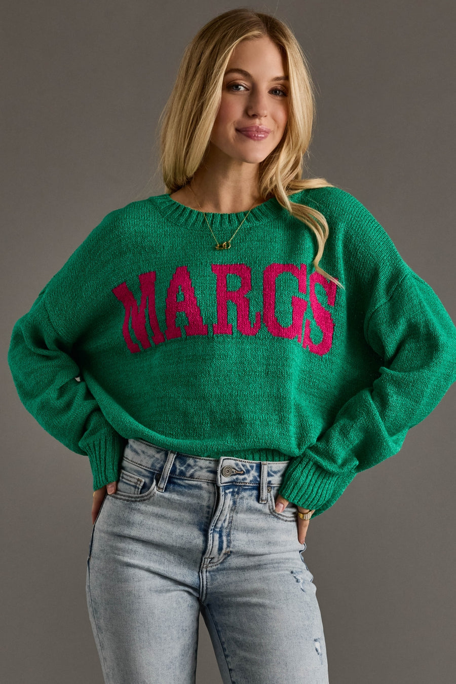 Woman wearing a green sweater with 'MARGS' in pink text against a gray background