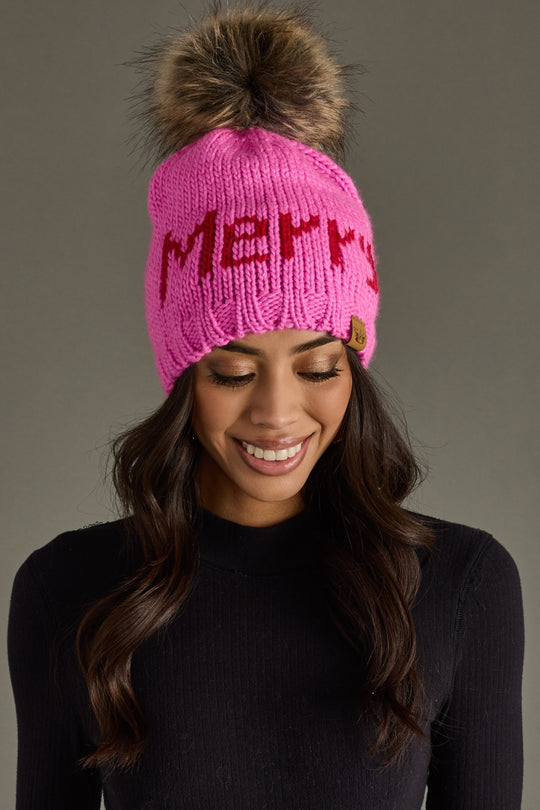 Woman wearing a pink knit hat with a fur pom-pom on a gray background