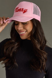 Person wearing a pink cap with 'Merry' embroidered on it against a neutral background