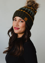 Woman wearing a green knit beanie with a pom-pom on a gray background