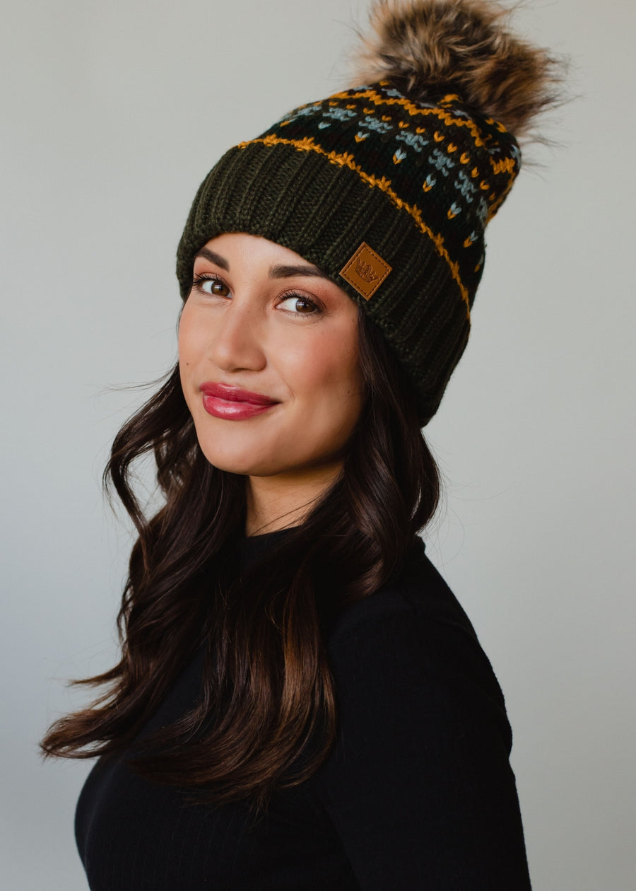 Woman wearing a green knit beanie with a pom-pom on a gray background