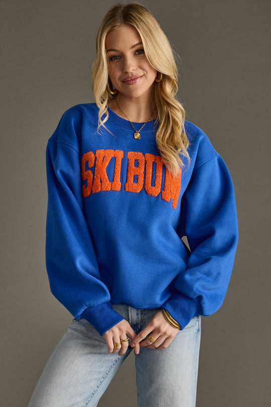 Person wearing a blue sweatshirt with 'SKIBUM' text on a gray background