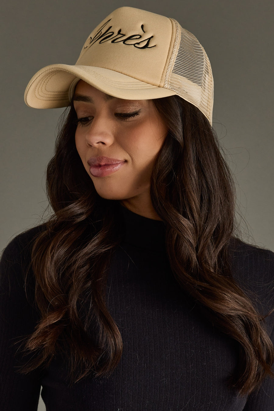 Woman wearing a beige cap with 'Apres' embroidery on a gray background