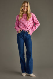 Woman wearing a pink sweater with text and blue jeans on a gray background