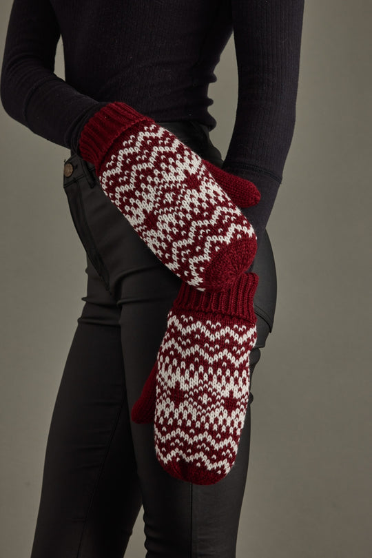 Person wearing red and white patterned mittens on a gray background