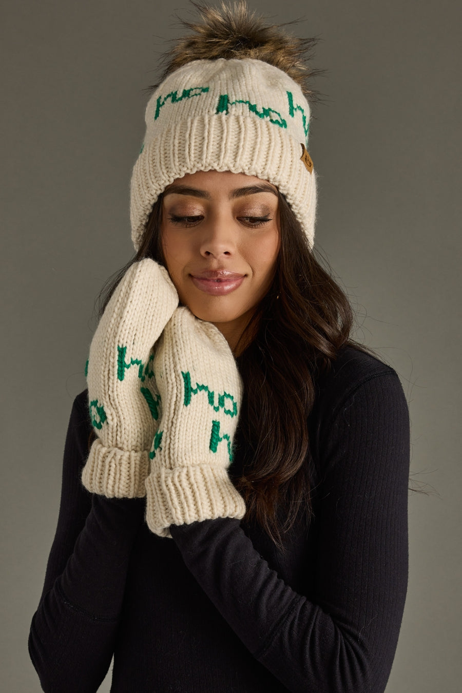 Woman wearing a cream knit hat and gloves with green text on a gray background