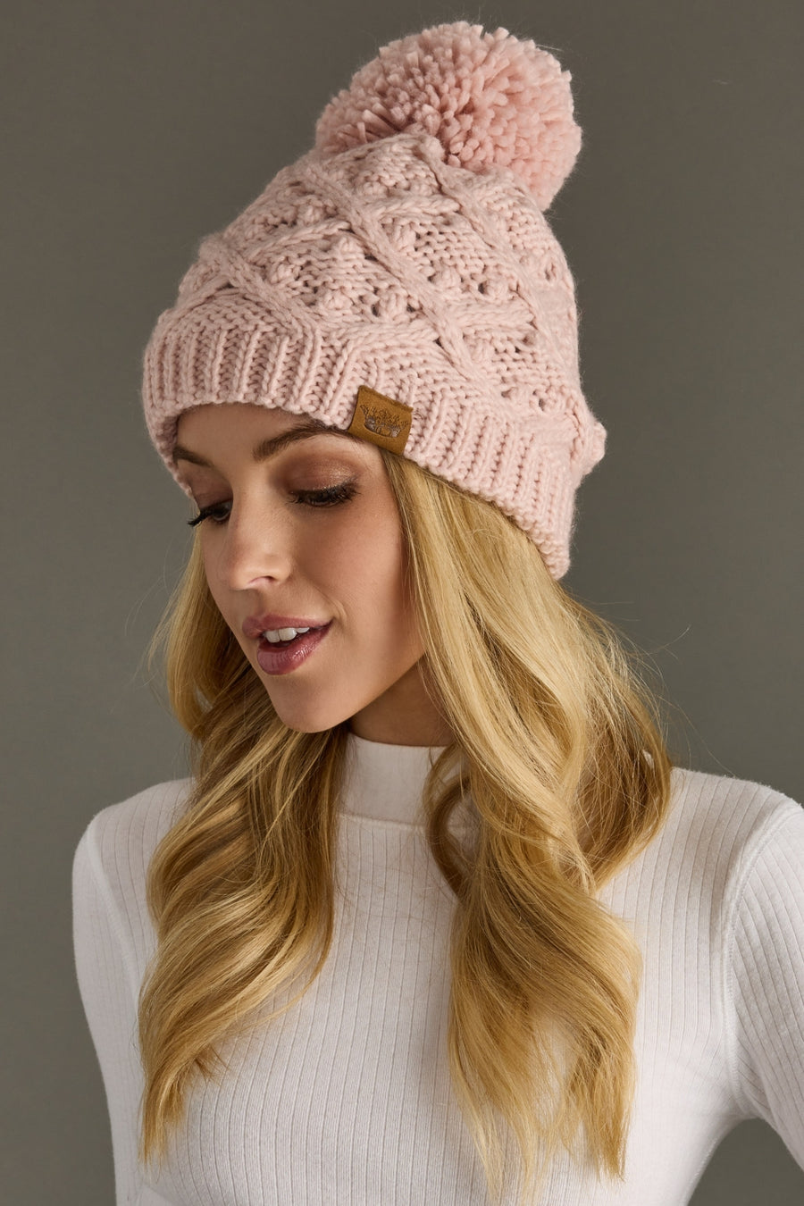 Woman wearing a pink knit beanie with a pom-pom on a gray background
