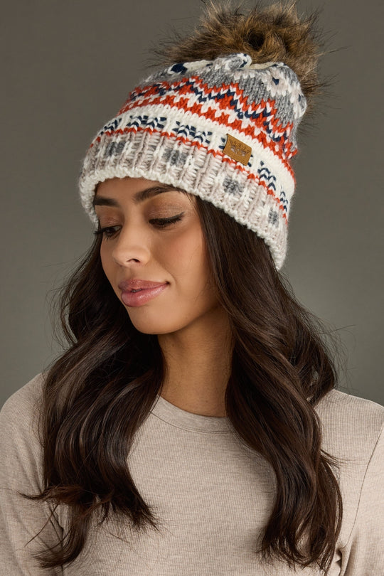 Woman wearing a patterned knit beanie with a fur pom-pom on a gray background