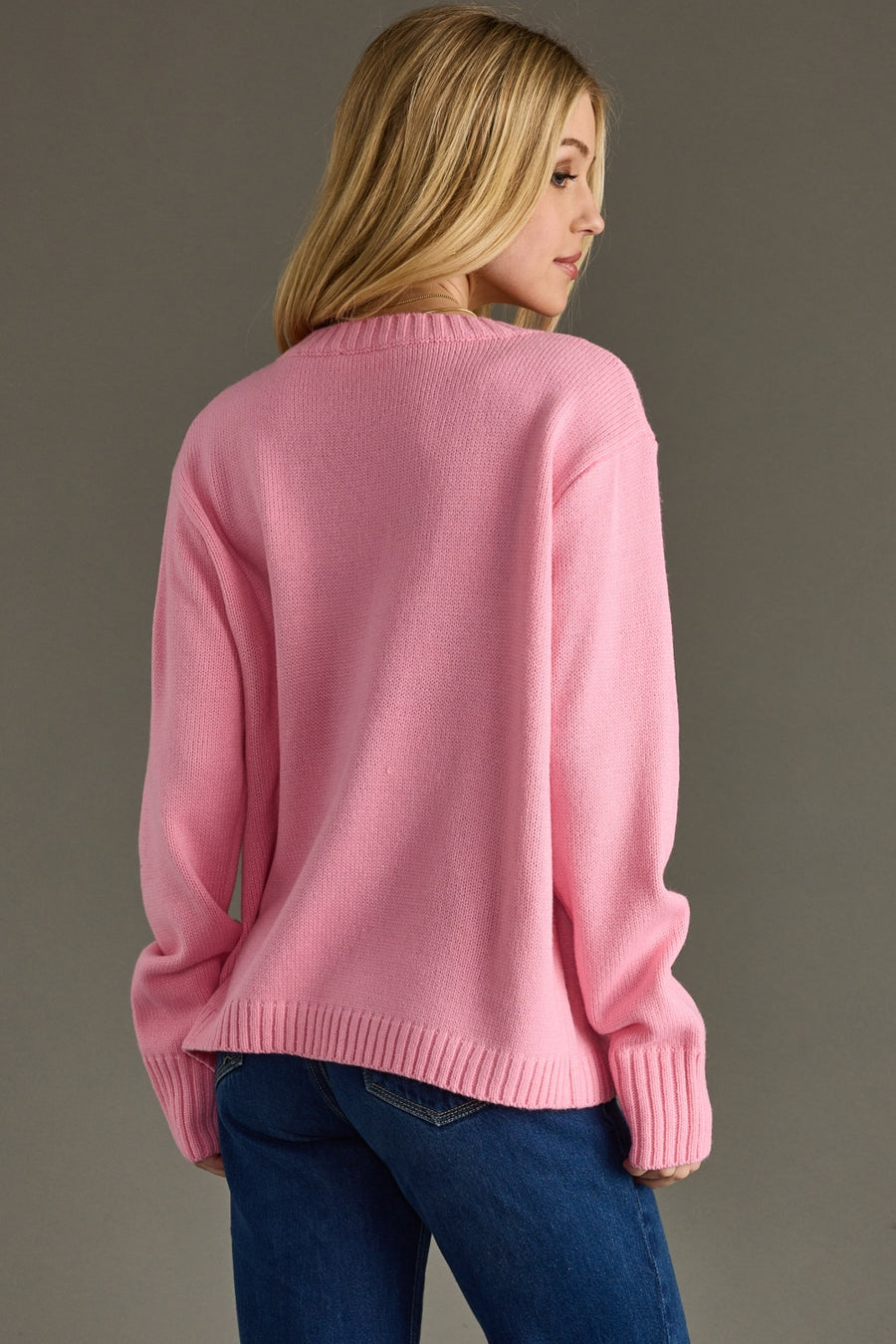 Person wearing a pink sweater and blue jeans against a gray background