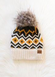 Knit beanie with a pattern and fur pom-pom on a white surface